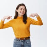 Happy woman pointing at herself in a yellow sweater, promoting home renovation services in the USA.